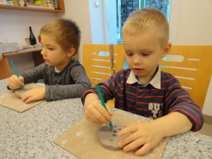 Fabian i Oliwier odciskają ołówkiem dziurki w ulepionym z gliny guziczku;-)